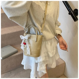 Détail d'un sac seau kaki avec nœud en dentelle et pendentif cerise par un mannequin