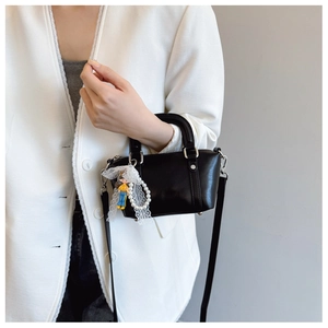 Detail of black leather handbag with white lace trim, pearl charm and doll pendant detail