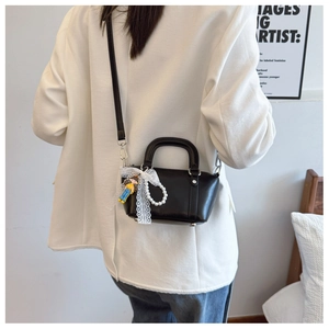 Close-up of black handbag featuring white lace bow, pearl charm, and cartoon doll pendant