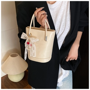 Détail d'un sac seau crème avec nœud en dentelle, perles et breloque cerise élégante