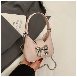 Détail du mini sac rose avec boucle nœud argenté sur fond de costume gris chic