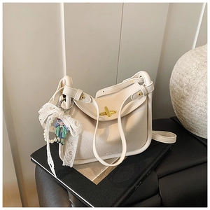 Detail of white lychee leather shoulder bag with gold metal twist lock and lace charm