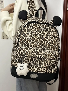 Leopard print backpack with 3D ears and plush pendant worn by a model in casual setting