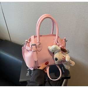 Close-up of pink litchi texture bag with plush dog charm and adjustable shoulder strap