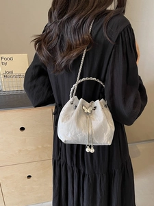 Sac seau en satin argenté avec papillon et glands de perles porté par le modèle