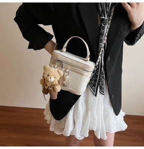 Détail d'un sac boîte blanc crème avec texture tressée, chaîne dorée et breloque ours