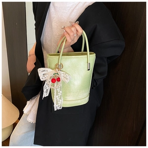Détail du sac seau vert clair avec breloques cerise, nœud en dentelle et perles