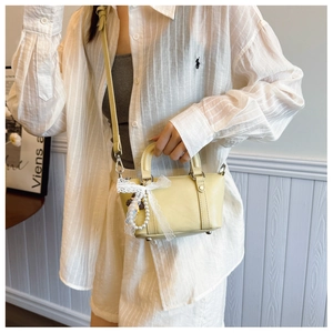 Close-up of yellow leather handbag with lace bow detail and pearl charm pendant