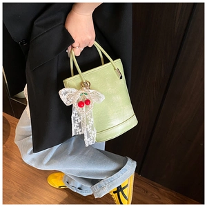 Détail du sac seau vert clair avec breloque cerise et nœud en dentelle blanche