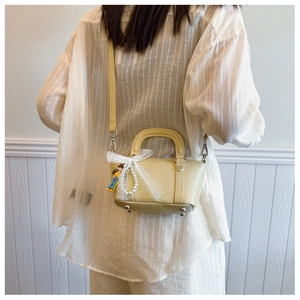 Rear view of model holding a beige mini Boston bag with lace bow and pearl charm