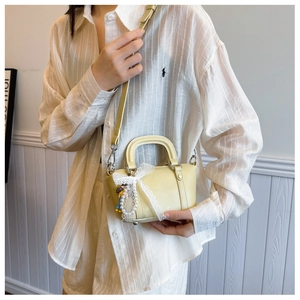 Detail of yellow mini Boston bag with white lace bow and pearl doll pendant