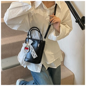 Sac seau noir avec nœud en dentelle blanche et cerises porté en bandoulière par un mannequin