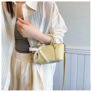 Detailed view of mini yellow leather handbag with lace bow and pearl charm worn by model
