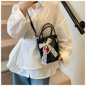 Détail du sac seau en cuir noir orné d'un nœud en dentelle blanche, perles et cerises