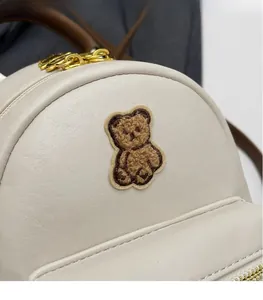 Détail du sac à dos blanc en similicuir texturé avec écusson d'ours en peluche et zip doré