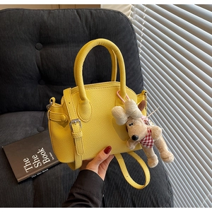 Detail of yellow lychee leather handbag with a cute plush puppy charm on a soft chair