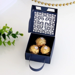 Detail of dark blue laser-cut cross favor box with golden chocolates for weddings