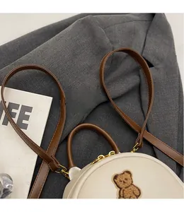 Détail de la bandoulière amovible et de l'écusson ours sur le sac en similicuir crème