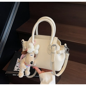 Detalle del bolso concha blanco roto con textura litchi y colgante de perro de peluche