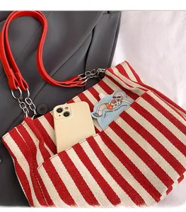 Détail du cabas à rayures rouges avec sangle en cuir, chaîne et poche avant pour téléphone
