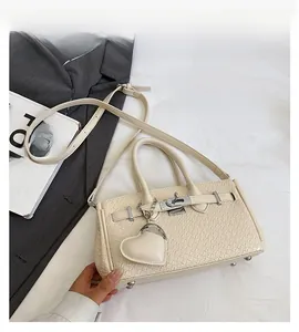 Detail of cream crocodile embossed handbag with metal lock and heart charm on a bed