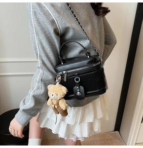Détail du sac vanity noir avec texture matelassée et charmant pendentif d'ours en peluche