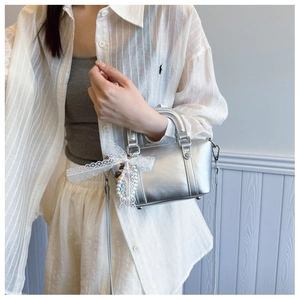 Silver metallic crossbody bag with lace bow and pearl charm detail worn by model