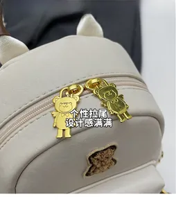 Détail des zips ours dorés sur sac à dos en cuir PU beige avec patch ours en peluche