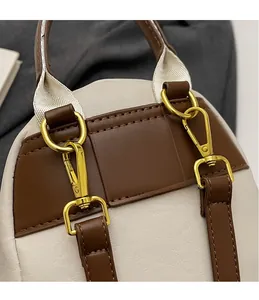 Vue détaillée des crochets dorés et des sangles en cuir PU sur un sac à dos bicolore