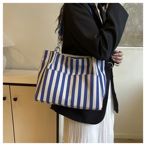 Détail d'un sac cabas en toile à rayures bleues et blanches avec bandoulières en cuir