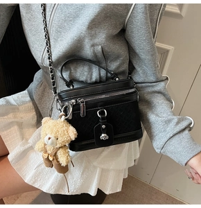 Détail d'un sac bowling noir avec texture tissée, pendentif ours et bandoulière en chaîne