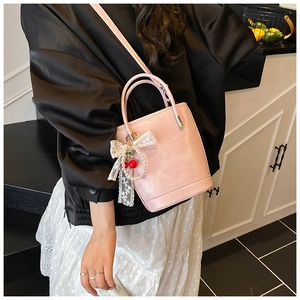 Détail du sac seau en cuir rose avec nœud en dentelle blanche et breloque cerise