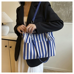 Détail du sac cabas en toile rayée bleue et blanche avec bandoulières dans une pièce
