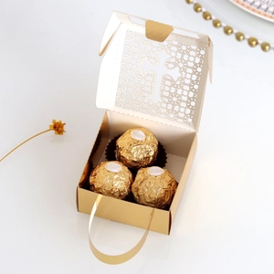 Detail of golden laser-cut cross wedding favor box with ribbon handle and chocolates