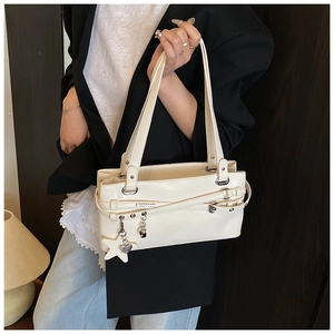Détail d'un sac sous le bras blanc crème avec boucles et pendentifs cœur étoile