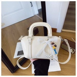 Detail of cream white leather handbag with lace bow and pearl charm accessories