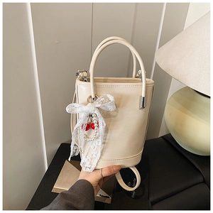 Détail du sac seau blanc cassé avec nœud en dentelle, perles et breloques cerise