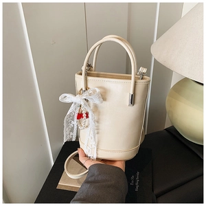 Détail du sac seau beige avec pendentif en dentelle, accents de cerise et de perles
