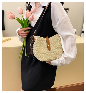 Detail view of woven straw shoulder bag with leather strap and decorative fringe