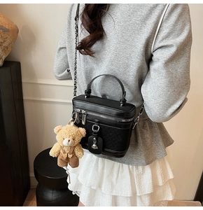 Détail du sac boîte noir avec texture tissée, bandoulière chaîne et breloque ours en peluche