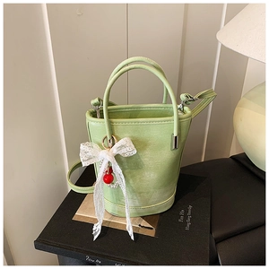 Détail du sac seau vert clair avec nœud en dentelle, perle et texture en cuir velouté