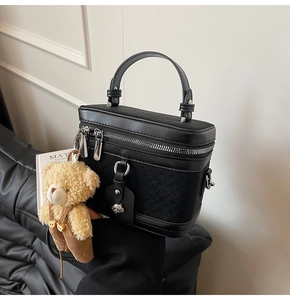 Détail du sac à main noir à texture tressée avec zip argenté et breloque ours en peluche