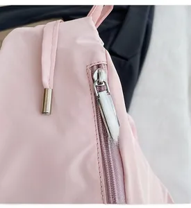 Detail of silver metal zipper pull on light pink nylon crossbody bag with glossy texture