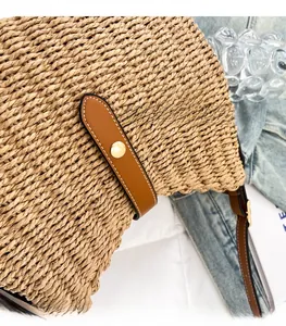 Close-up of handwoven straw bag featuring brown leather trim and golden metal snap buckle