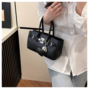 Close-up of black woven texture bag featuring a heart pendant and elegant metal lock clasp