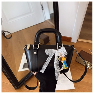 Close-up of black oil wax leather handbag with large lace bow and pearl chain detail