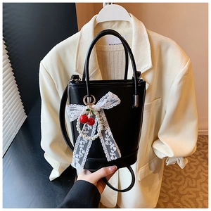 Détail du sac seau noir en cuir avec nœud en dentelle blanche, perles et cerises