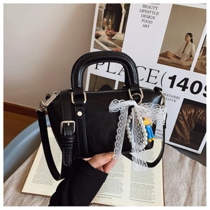 Detail of black leather Boston bag with lace bow, pearl chain and doll charms