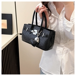 Detail of black woven texture handbag with silver turn-lock and heart charm accessory