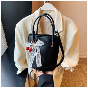 Détail du sac seau en cuir noir avec nœud en dentelle blanche et pendentif perle